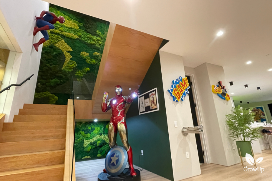 A custom green moss wall frames a luxury Los Angeles residential staircase featuring a life-sized Iron Man statue and a Spider-Man figure climbing the wall.
