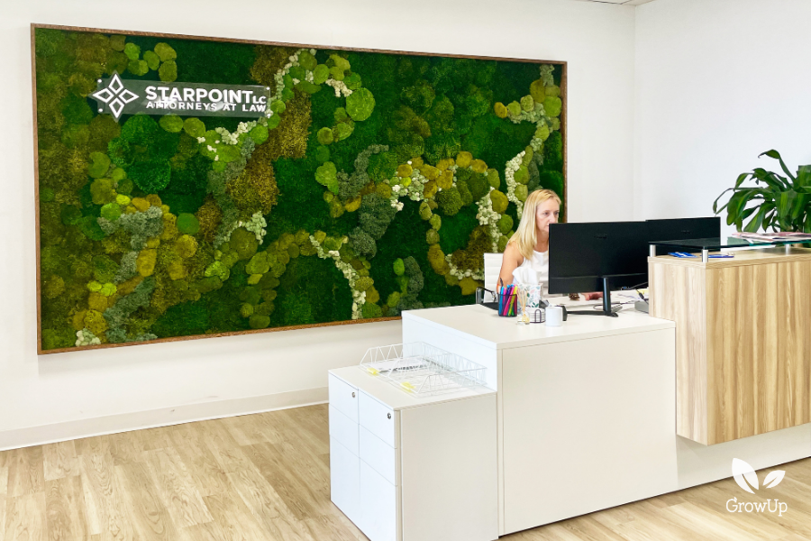 A corporate office reception desk with an employee working at a computer, set against a large, framed feature wall made of multi-textured green and white preserved moss with the Starpoint Attorneys at Law logo.