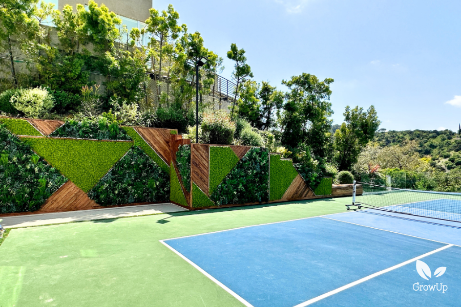 High-end residential landscaping featuring a geometric wood and green wall installation alongside a private outdoor tennis court in Los Angeles.