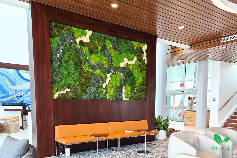 A large corporate biophilic moss art installation featuring intricate patterns of dark green, light green, and white preserved moss behind a seating area.