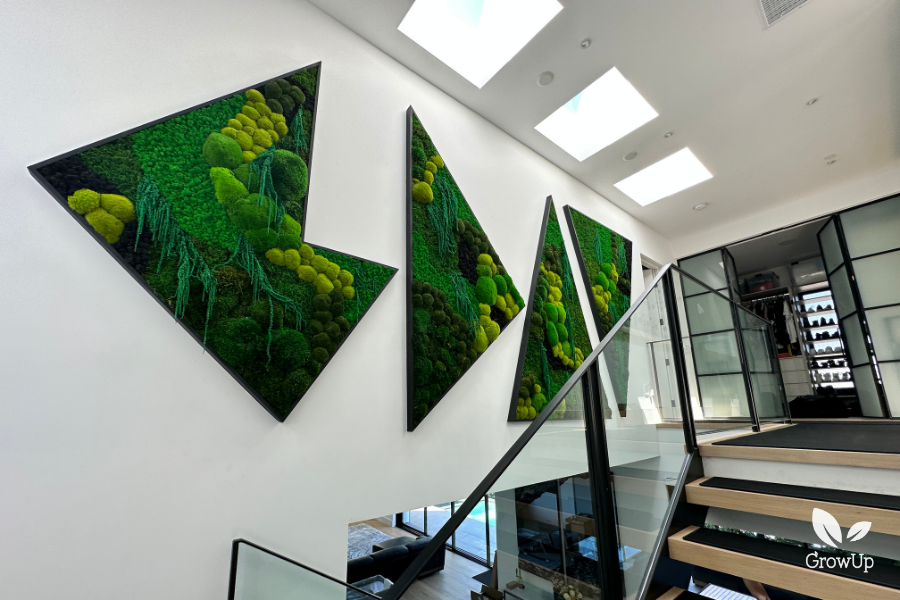 Four custom geometric, chevron-shaped green moss wall panels installed under skylights along a modern residential glass staircase.