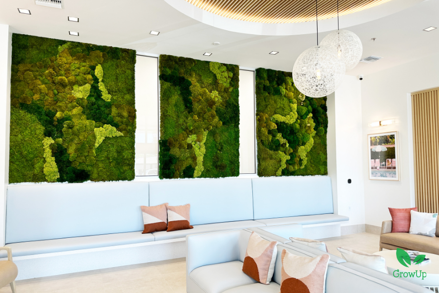 A modern lobby with three large rectangular moss art panels in shades of green mounted on a white wall above a long, light-blue bench.
