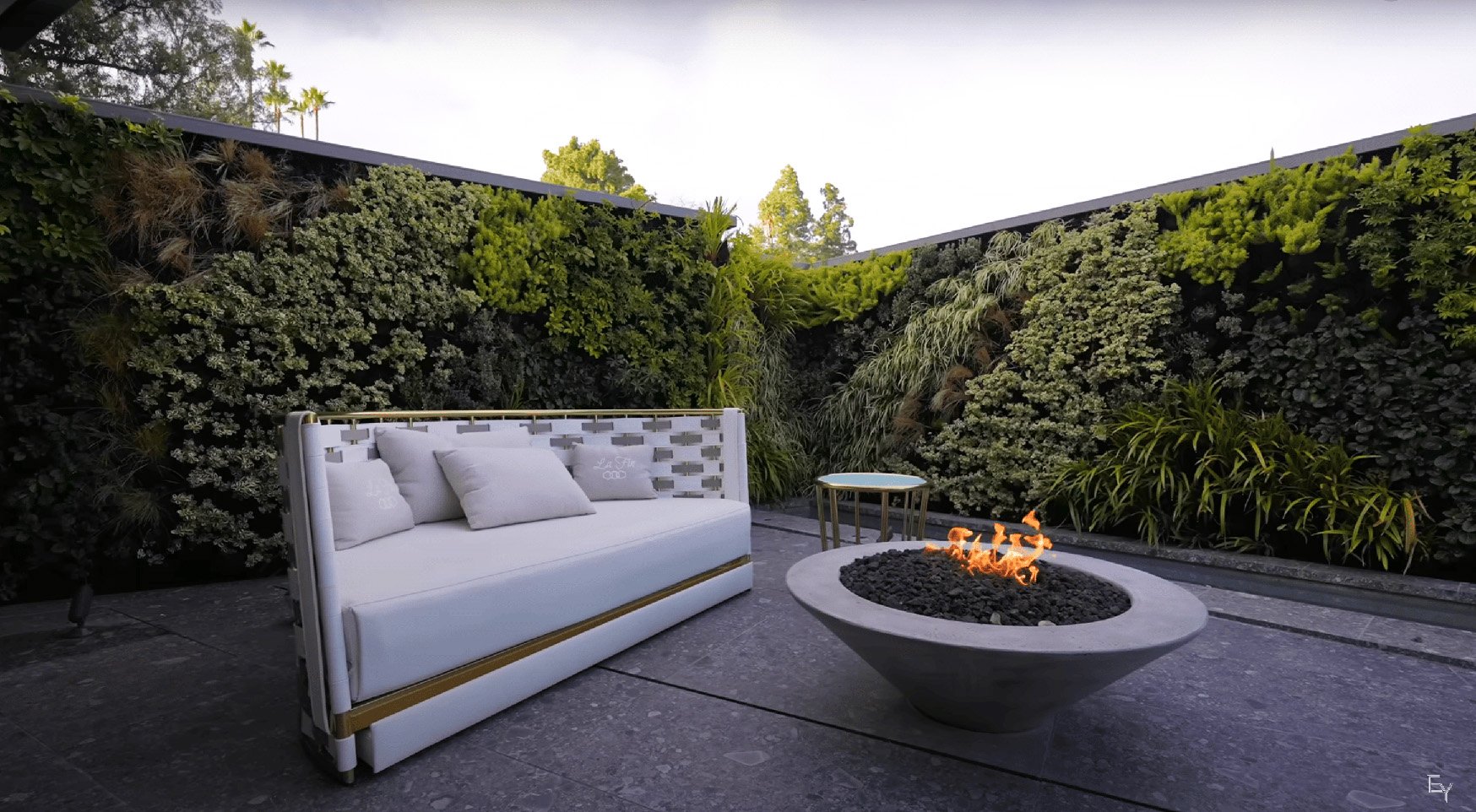 Outdoor living wall wrapping a Bel Air terrace with a built-in sofa and a round fire bowl at dusk