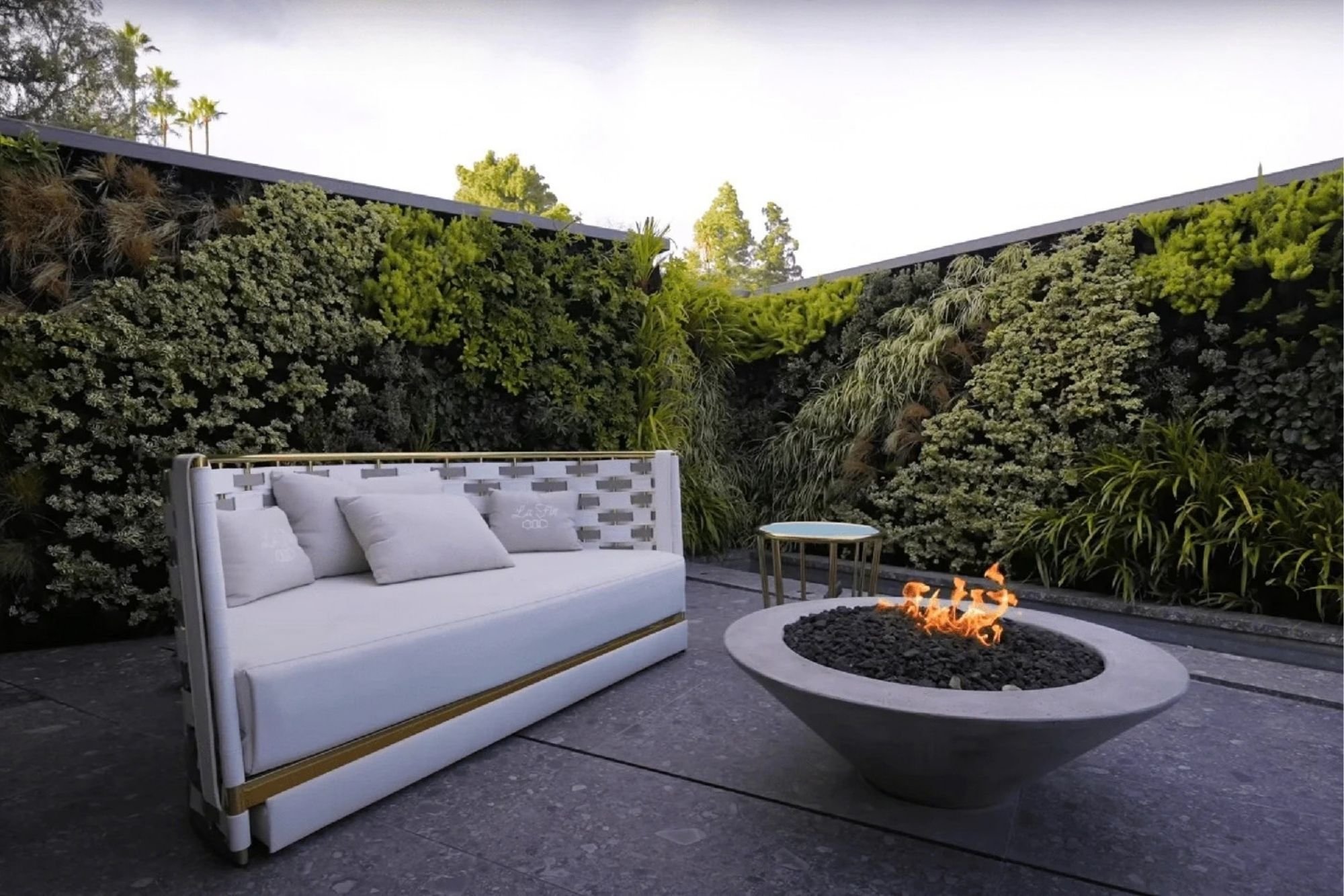 Outdoor living wall wrapping a Bel Air terrace with a built-in sofa and a round fire bowl at dusk