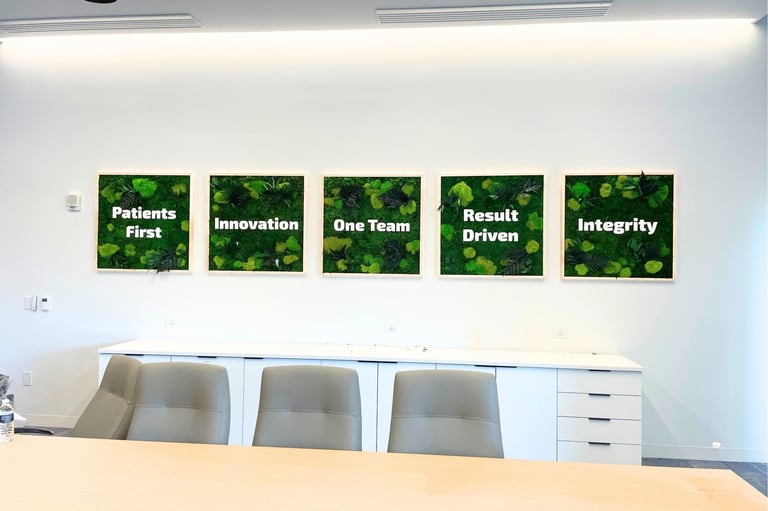 Five 3 ft by 3 ft moss walls in a row on a conference room wall, each lettered with a company value