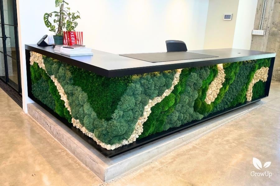 A modern L-shaped reception desk with its front panels decorated in an organic, flowing pattern of green and white textured moss.